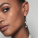 A model wearing Juraster’s 9ct White Gold Diamond Hoop Earring, Anchor, crafted from Fairmined white gold and conflict-free diamonds. She also wears two white gold diamond studs, one in her tragus and one in her second and a white gold diamond tassel earring charm.