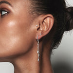 A model wearing Juraster’s 9ct White Gold Diamond Hoop Earring, Anchor, crafted from Fairmined white gold and conflict-free diamonds. She also wears two white gold diamond studs and a white gold diamond tassel earring charm.