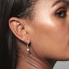 A model wearing Juraster’s 9ct White Gold Diamond Hoop Earring, Anchor, crafted from Fairmined white gold and conflict-free diamonds. She also wears a sterling silver hoop in her tragus and a sterling silver pearl earring charm.