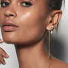 A model wearing Juraster’s 9ct Gold Diamond Hoop Earring, Anchor, crafted from Fairmined yellow gold and conflict-free diamonds. She also wears two yellow gold studs, one diamond and one pearl, along with two yellow gold earring charms, one a dangle and one pearl.