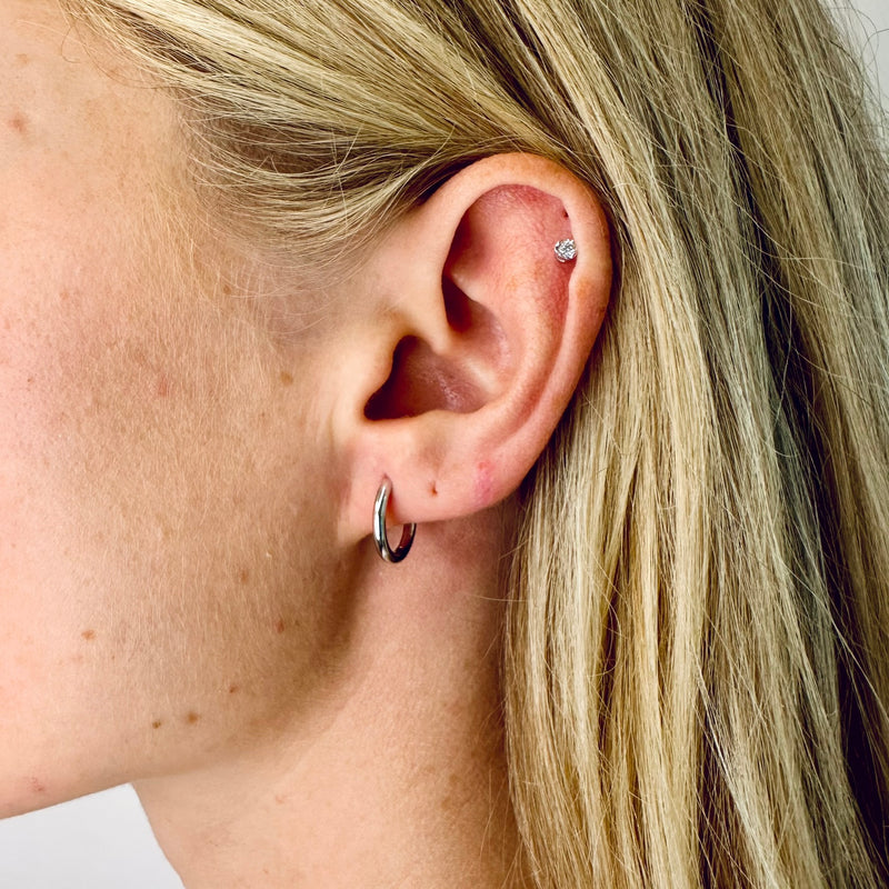 A model wearing Juraster’s Sterling Silver Classic Hoop Earring, Anchor, crafted from Fairmined sterling silver and a white gold diamond stud.