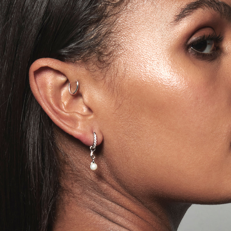 A model wearing Juraster’s Sterling Silver Akoya Pearl Earring Charm, Beachcomber, crafted from Fairmined sterling silver and a responsibly-farmed pearl, attached to a white gold pavé diamond hoop and a sterling silver hoop in her forward helix.