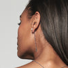 A model wearing Juraster’s Sterling Silver Dangle Earring Charm, Discovery, crafted from Fairmined sterling silver, alongside a sterling silver diamond-shaped earring charm, attached to a sterling silver pearl earring stud. She also wears a white gold diamond stud in her tragus and a sterling silver necklace.