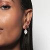 A model wearing Juraster’s 9ct Gold Classic Diamond Stud Earring, Light-Ray, crafted from Fairmined yellow gold and conflict-free diamonds. She also wears a yellow gold hoop in her tragus, two yellow gold studs, one labradorite and one diamond, with two yellow gold earring charms, one rainbow moonstone and one diamond-shaped.