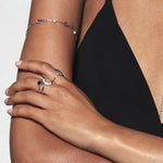 A model wearing Juraster’s Sterling Silver Stacking Ring in Black Onyx, Lodestone, crafted from Fairmined 9ct sterling silver and a hand-cut black onyx gemstone. She also wears two diamond-shaped rings, one sterling silver and one white gold diamond encrusted, alongside a sterling silver pearl bracelet.