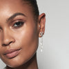 A model wearing Juraster’s 9ct White Gold Diamond Tassel Earring Charm, Palace, crafted from Fairmined white gold and conflict-free diamonds, and a white gold diamond earring jacket attached to a white gold diamond stud, along with a white gold diamond stud in her tragus.