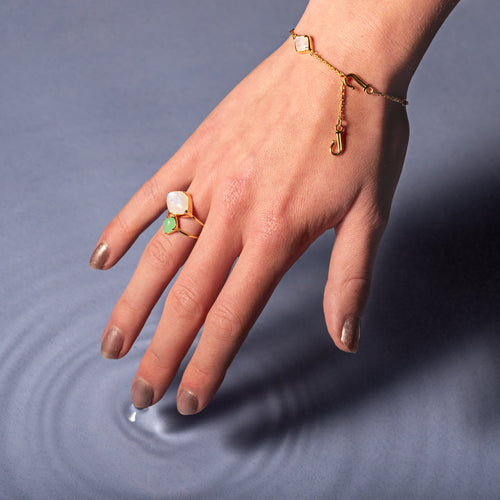 A model wearing Juraster's 9ct Gold Rainbow Moonstone Adjustable Bracelet, Three Wishes, crafted from Fairmined 9ct yellow gold and hand-cut rainbow moonstones. She also wears chrysoprase and moonstone yellow gold rings.