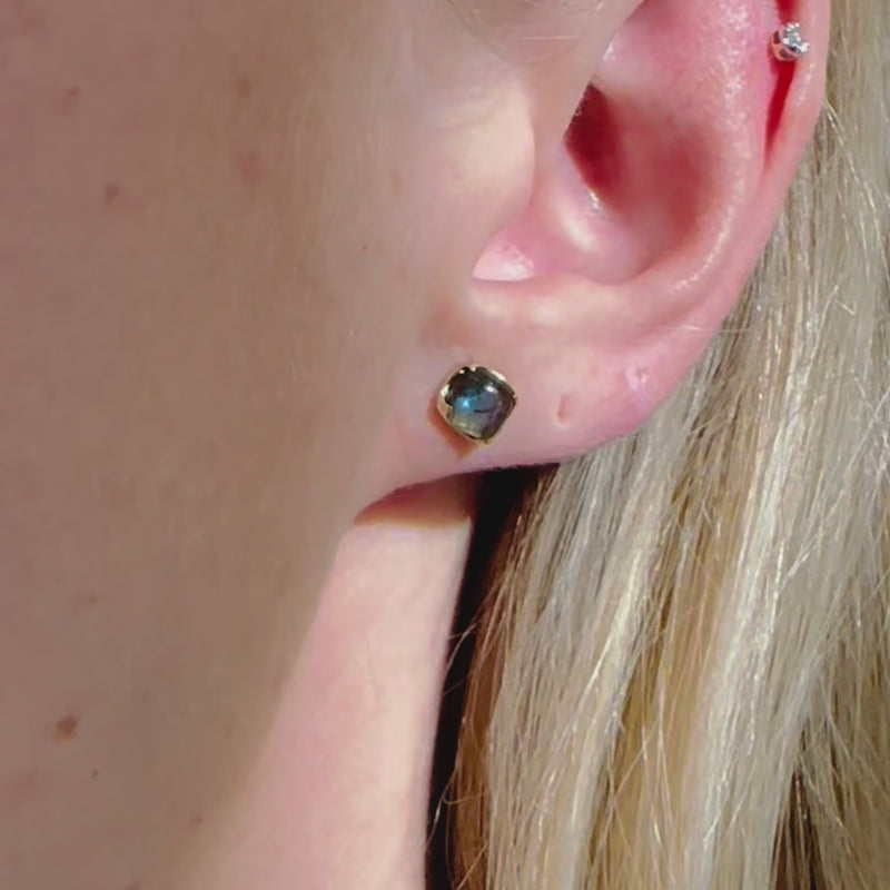 A video of a model wearing Juraster’s 9ct Gold Blue Labradorite Stud Earring, Adventure, crafted from Fairmined yellow gold and hand-cut blue labradorites, along with a yellow gold diamond stud in her cartilage.